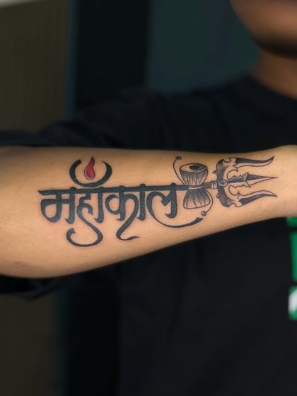 A popular Mahakal name tattoo design for the forearm. The lettering is stylized to include the trishul and damaru, making it a favorite among devotees.