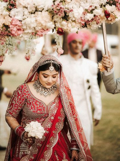 The bride's grand entrance. Walking under a 'phoolon ki chadar' held by her loved ones, her serene expression is full of grace and anticipation.