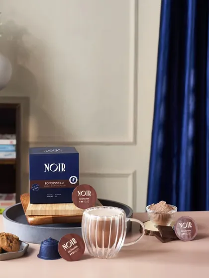 A styled shot for the coffee brand NOIR, featuring their hot chocolate pods. The deep blue and pink tones create a luxurious and modern feel, aligning with the brand's premium positioning.