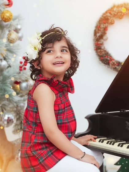 A little girl plays the piano in front of the Christmas tree. Our holiday setups include fun props to create a variety of festive scenes.