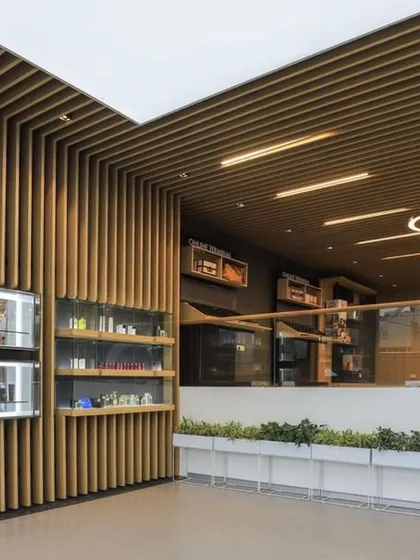 The reception and product display area at the Oriflame office, featuring modern circular light fixtures and vertical wood slats. The design is clean, bright, and reflects the brand's natural wellness identity.