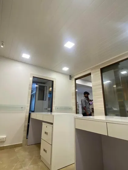 A wide view of a completed office for a Chartered Accountant client. This angle highlights the clean, open layout with custom-built modular desks, integrated drawers, and a modern PVC panelled ceiling with recessed LED lighting. The design focuses on creating a professional and efficient workspace.