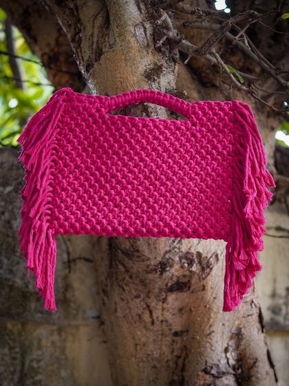 This 'Pink Popper' macrame bag is for those who love to make a statement! The vibrant pink color is so eye-catching, and the side fringe adds a playful touch. It's a spacious handbag with a detachable strap, perfect for any occasion.