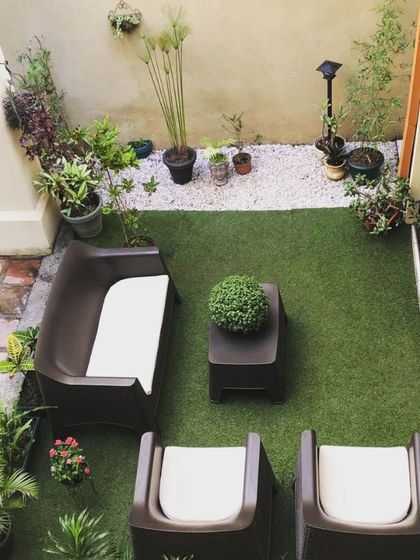An aerial view of a simple yet effective terrace layout. I used high-quality artificial grass to define a seating area with modern outdoor furniture, surrounded by a border of white pebbles and potted plants for a neat and tidy look.