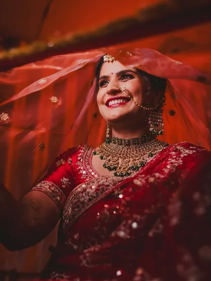 The joy of a North Indian bride is absolutely infectious. This candid shot captures her genuine happiness, with the vibrant red of her veil creating a classic and timeless bridal portrait that radiates warmth and excitement.