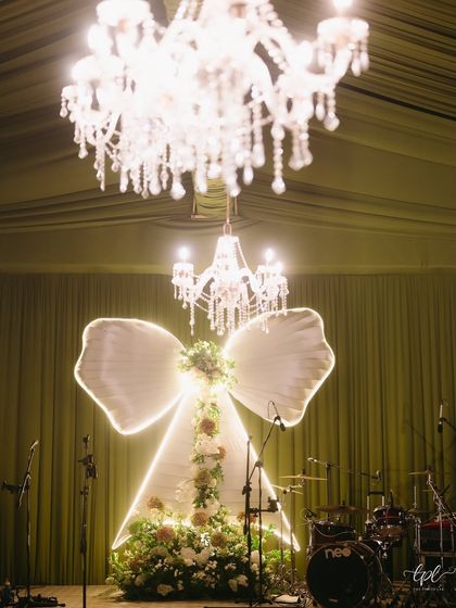 The statement backdrop for "The Big Bow Affair." A giant, illuminated bow structure filled with flowers served as the focal point for the stage, perfectly capturing the event's modern fairytale theme.