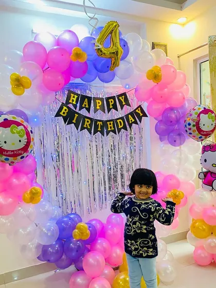 A happy moment from a 4th birthday party we photographed. This image shows the birthday girl posing in front of a custom Hello Kitty themed balloon arch and shimmer backdrop we designed for her special day at home.
