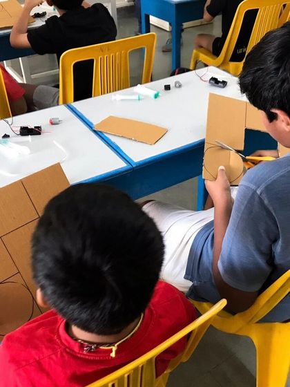 Kids at Vidya Niketan School work on building a model of a disc brake using cardboard and syringes. It's a hands-on way to learn about hydraulics.