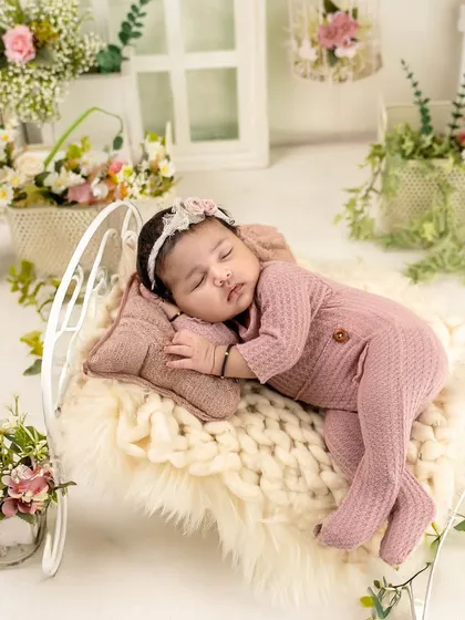 Sweet dreams on a tiny bed. This newborn is dressed in a cozy pink outfit, sleeping on a miniature bed adorned with beautiful flowers.
