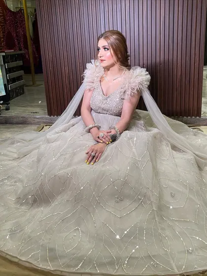 A seated portrait in our beige bustier ball gown. The shimmer tulle fabric, embellished bodice, and dramatic feather and ruffle sleeves create a look of pure luxury and sophistication.