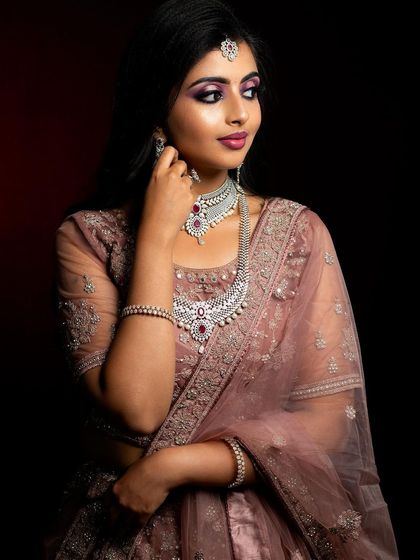 This North Indian bridal look features a soft, dusty rose lehenga paired with diamond jewelry. The makeup focuses on a subtle smokey eye and a matching lip color for a modern yet traditional feel.