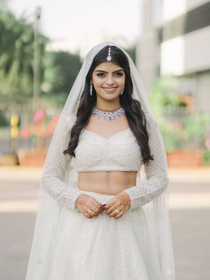 A beautiful outdoor portrait of the bride in her white lehenga and veil. Her bright smile and the clean, simple background make this a fresh and modern bridal shot.