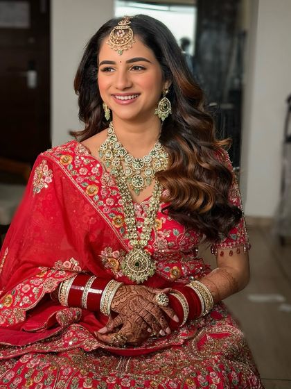 A full portrait of the bride, looking radiant and confident. The open, wavy hairstyle adds a modern touch to her traditional red bridal look.