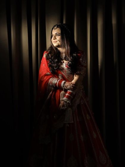 A dramatic and artistic portrait of the bride. The play of light and shadow highlights the rich color and intricate embroidery of her traditional red wedding lehenga.