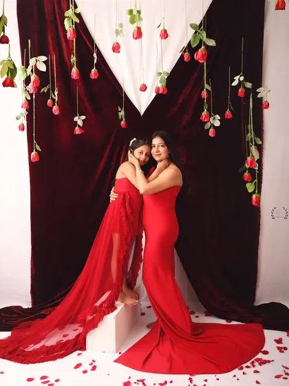 A beautiful full-length portrait of a mother and daughter in matching red gowns. The flowing fabric and romantic Valentine's setup create a stunning and elegant image.