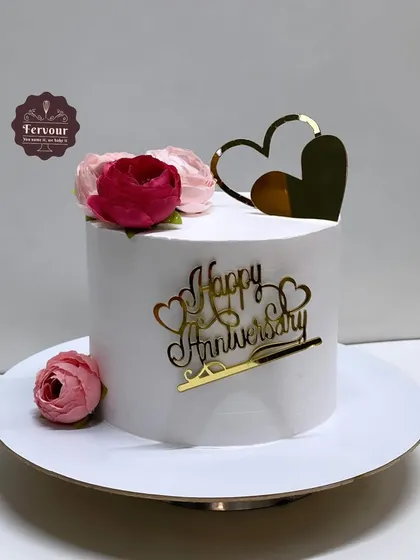 A simple yet elegant anniversary cake. This fresh fruit cake has a clean white finish and is topped with a gold "Happy Anniversary" topper and a few delicate flowers.
