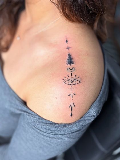 A minimalist symbolic tattoo on the shoulder, featuring an evil eye, a tree, and other elements. It's a personal story told through simple lines.