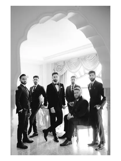 An elegant black and white portrait of the groom and his crew. Their formal suits and confident poses, framed by a palace archway, create a timeless and sophisticated image.