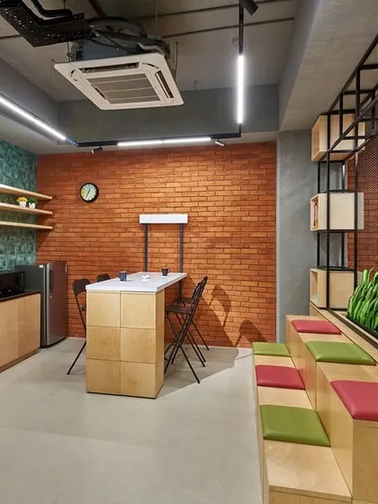 A closer look at the amphitheater seating and pantry area within the reception. The design combines plywood, exposed brick, and green tile for a textured, eclectic, and highly functional entrance space.