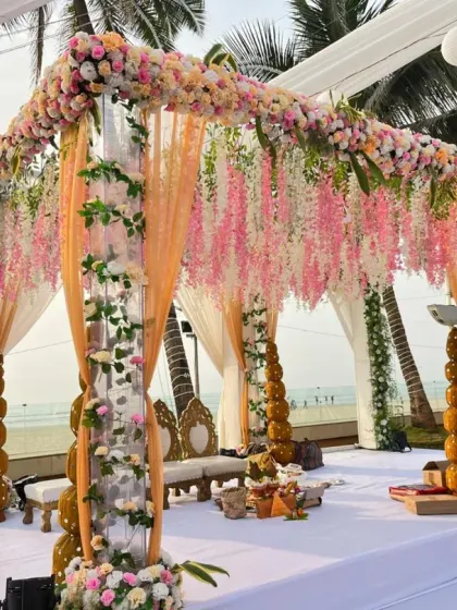 A stunning mandap design featuring hanging floral chandeliers and delicate vines. The combination of peach drapes and white flowers against the beach backdrop creates a truly romantic and high-end look.