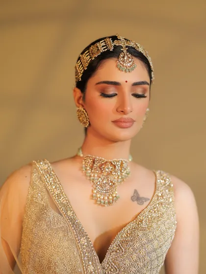 An eyes-closed portrait capturing a moment of serenity. The styling highlights the soft, glowing makeup that complements the golden ensemble.