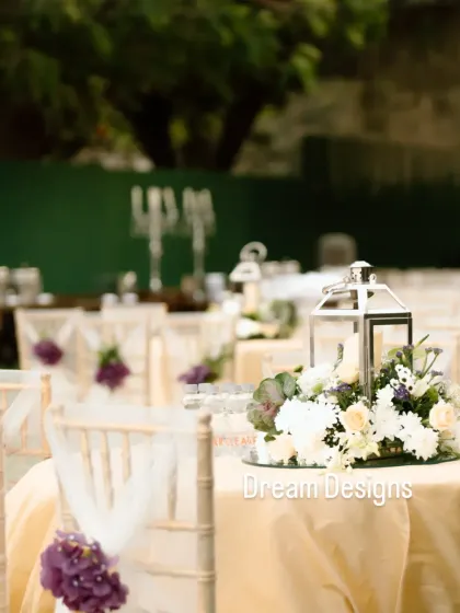 A simple yet elegant table setting. The centerpiece combines white and purple flowers with a classic silver lantern, creating a sophisticated look for this outdoor wedding.