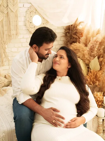 An intimate couple's portrait filled with affection. The couple sits together on a bed in a boho-chic setting, looking into each other's eyes with loving smiles.