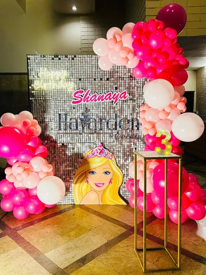 A fun Barbie-themed party with a silver sequin backdrop and a vibrant pink balloon garland. The Barbie head cutout is a great photo prop.