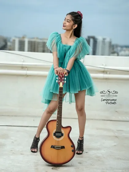 A full-length shot of the model posing with her guitar on a rooftop, blending a chic dress with a musical passion.
