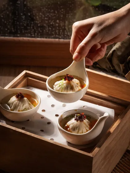Soup dumplings (xiao long bao) served in individual spoons. This action shot captures the moment of serving, highlighting the delicate nature of the dish.