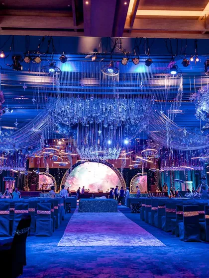 A wide shot of a celestial-themed event hall, bathed in blue light. The decor includes hanging installations that mimic stars and galaxies, creating a fully immersive environment.