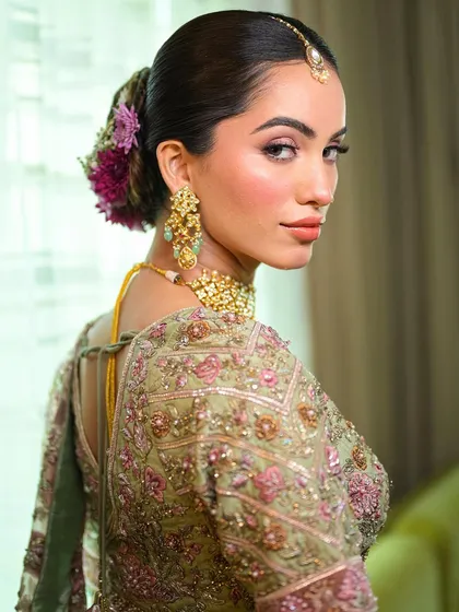 The delicate embroidery of the lehenga is mirrored in the soft, detailed makeup. This look from the back shows how the floral hairstyle and glowing skin come together for a cohesive, beautiful bridal style.