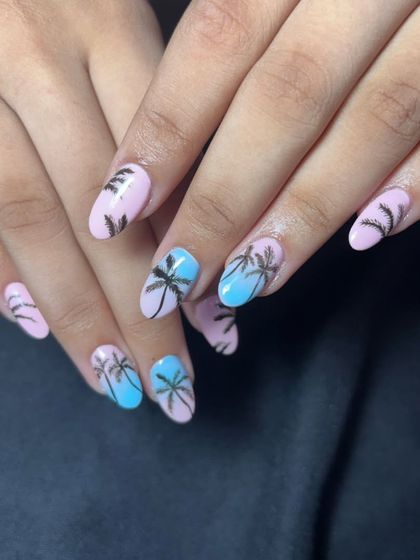 Get into a summer mood with these beach-themed nails. The design features a pink and blue base with hand-painted black palm tree silhouettes.