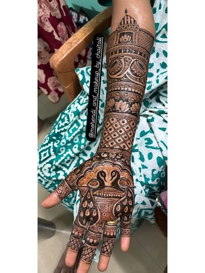 A single arm view of a bridal mehendi, showcasing the combination of peacock figures on the hand and architectural motifs on the forearm.