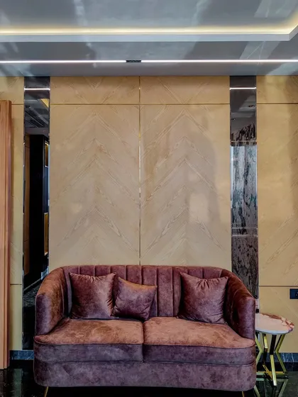 A full view of the seating area in Mr. Sameer's cabin, featuring a plum-colored sofa against a wall of light wood veneer and mirrored strips. The design creates a comfortable yet formal space for discussions.