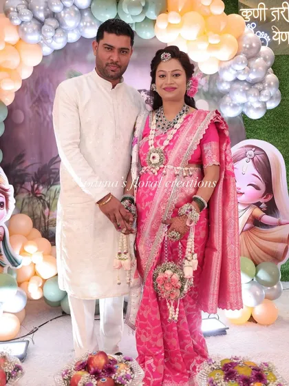 A lovely couple posing at their baby shower event. She is wearing a pink and white floral jewellery set with a matching floral purse.