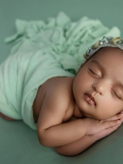 A close up of the baby's sweet face, with the floral headband adding a lovely detail against the soft green background.