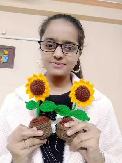Here I am, the daughter of the duo, holding two of our classic sunflower pots. I handle the designs, social media, and packing, while my mom is the master crocheter.