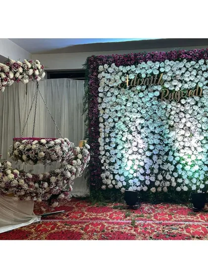A stunning floral naming ceremony setup. The decor features a beautiful crescent-shaped floral swing and a full flower wall in shades of white and purple, creating an elegant and memorable photo backdrop for the special occasion.