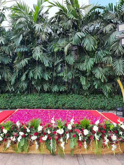 A simple yet impactful stage decoration with a bed of vibrant pink rose petals, bordered by red and white flowers against a lush green backdrop.
