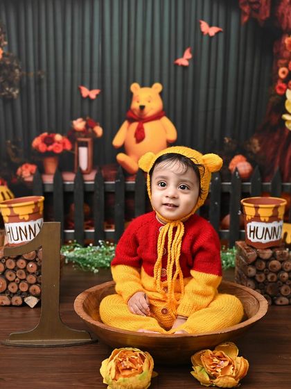 A sweet portrait of a baby boy dressed as Winnie the Pooh, sitting in a wooden bowl. The warm, earthy tones of the Hundred Acre Wood theme create a cozy and nostalgic feel.