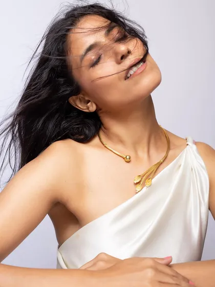 An expressive portrait featuring a modern, leaf-inspired gold choker. The wind-blown hair and joyful expression create a feeling of freedom and elegance for this western jewelry piece.