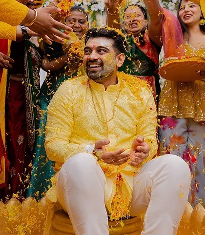 The groom enjoying his Haldi ceremony as friends and family shower him with petals and blessings. A moment of pure, candid fun.