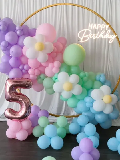 A sweet and cheerful daisy theme for a fifth birthday. I used pastel balloons in purple, pink, green, and blue to create a floral arch on a gold ring, with a large number '5' foil balloon.