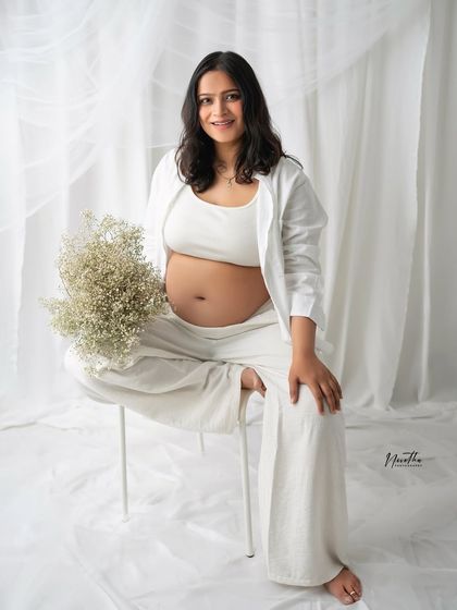 A serene maternity portrait. The mom-to-be is seated, holding a bouquet of baby's breath, creating a peaceful and classic image.