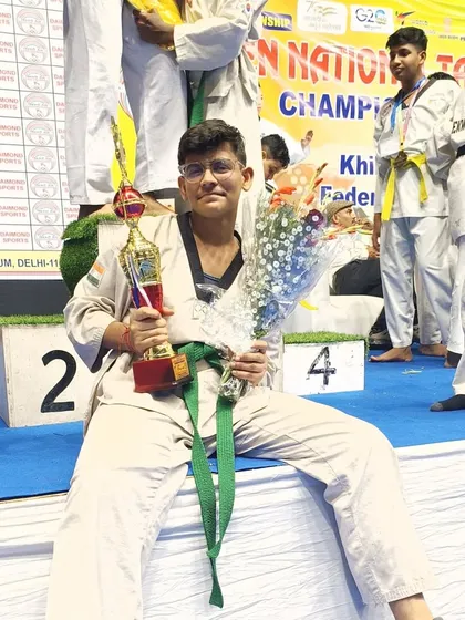 A student relaxing on the podium after his win, holding his trophy and flowers.