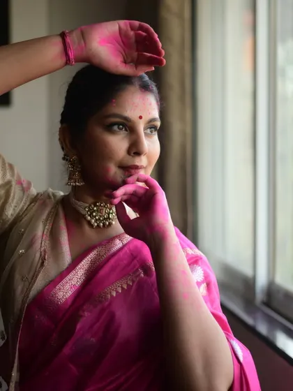 A candid moment from a Holi photoshoot, looking out a window. The natural light and subtle color on the skin create a soft, beautiful portrait.