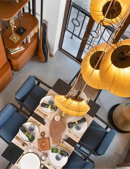 An aerial view of the dining area, highlighting the dramatic double-height ceiling. A cluster of large, dandelion-inspired pendant lights creates a stunning focal point over the dining table, adding warmth and a touch of whimsy to the space.