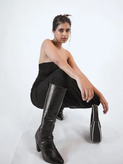 A full-body squat pose that is both edgy and powerful. This shot showcases the entire look, from the strapless dress to the knee-high leather boots, against a clean white backdrop.