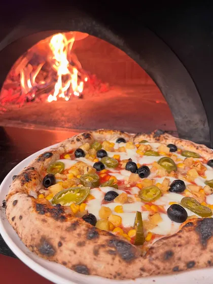 A veggie-loaded pizza in front of the flames. The intense heat cooks the toppings quickly, keeping them fresh and flavourful.